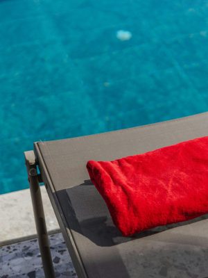 Red towel on sun lounger by a sparkling swimming pool, perfect for summer relaxation.