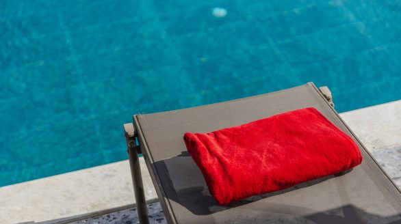 Red towel on sun lounger by a sparkling swimming pool, perfect for summer relaxation.