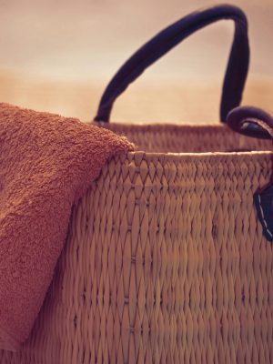 A straw beach bag with a towel draped over it, perfect for a summer day at the shore.