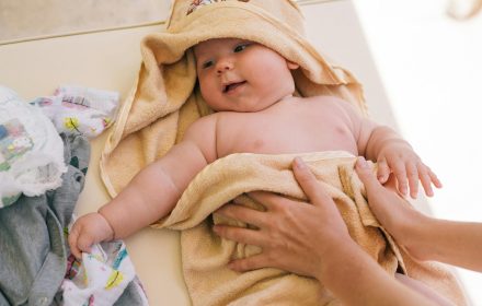 pexels photo 4668938 4668938 Cute newborn baby wrapped in a soft towel, smiling and feeling cozy indoors.